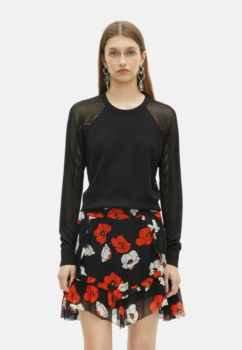 Maglione nero a maglia con maniche in rete, abbinato a una gonna nera con motivi floreali rossi e bianchi e volant lungo l'orlo.