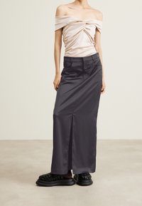 Off-shoulder satin beige topp med hög midja svart maxikjol med framfall och svarta vävda platåsandaler.