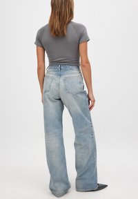Ljust blå högmidjade jeans med vida ben, med en blekt tvätt och bakfickor, i kombination med en figurnära grå kortärmad topp.