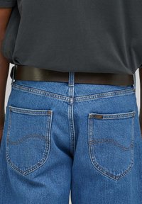 Blaue Jeans mit geradem Schnitt, ausgestattet mit zwei Gesäßtaschen mit gebogener Naht und einem braunen Ledergürtel in der Taille.