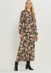 Sukienka maxi z czarnego materiału w beżowy kwiatowy wzór, z długim rękawem, kołnierzykowym designem, talią ściągniętą i zwiewną sylwetką, zestawiona z czarnymi botkami.