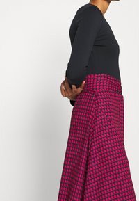 Svart långärmad topp i kombination med en kjol i rosa houndstooth-mönster. Kjolen har en bred midjeresår och flytande tyg.