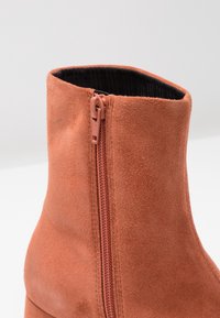 Suede enkellaars in terracotta kleur met een zijrits en een ribbelige, zwarte binnenvoering. Gladde textuur met een aansluitend ontwerp.