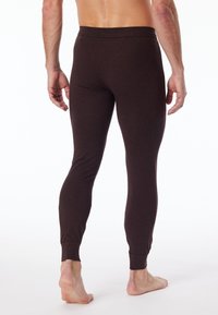 Braune, enganliegende Leggings aus weichem Stoff mit glatter Textur, ausgestattet mit einem breiten Taillenbund und schmal zulaufenden Bündchen an den Knöcheln.