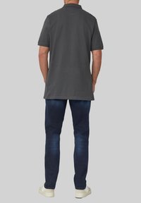 Szara koszulka polo z krótkim rękawem, prostym kroju i kołnierzykiem, zestawiona z ciemnoniebieskimi dżinsami i jasnymi sneakersami.