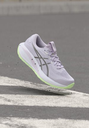 Chaussure de course violet clair avec semelle vert néon flottant au-dessus d'une rue avec des marquages routiers blancs.