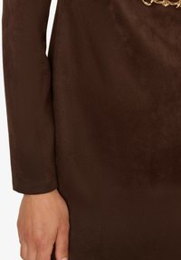 Hnědá semišová tkanina s měkkou texturou a dlouhými rukávy, s detailem zlatého řetězu v oblasti pasu pro lepší akcentaci.