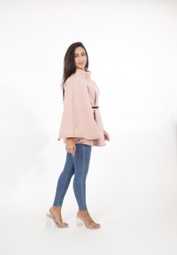 Ljust rosa, oversized cape-topp med hög krage och knappdetalj, ihop med denim leggings och genomskinliga blockklack-sandaler.