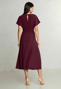 Dzintarkrāsas midi kleita ar īsām plandošām piedurknēm, atvērumu mugurpusē, zvana formas svārkiem un nēsāta ar kailām potīšu siksniņu papēžām. Gluda tekstūra.