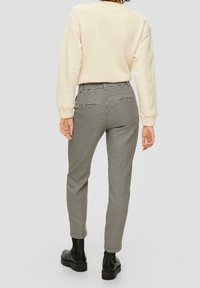 Sweatshirt beige clair avec des manches texturées, associé à un pantalon à carreaux noir et blanc taille haute. Des bottines noires viennent compléter la tenue.