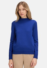 Blå jumper med hög krage, långa ärmar och ribbade manschetter. Tillverkad av ett mjukt stickat tyg med en bekväm passform.