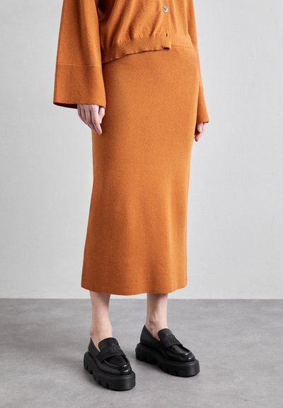Pletený oranžový cardigan a odpovídající sukně až po kotníky vyrobená z jemné vlněné směsi; v kombinaci s robustními černými mokasíny se strukturovanou podrážkou.