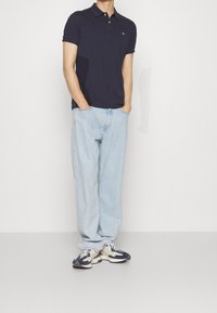 Marinblå pikétröja med kort ärm, har en krage och logotyp. Kombinerad med ljusblå baggy jeans och mörka sportskor.