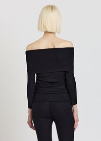 Schwarzer, schulterfreier, gerippter Pullover mit langen Ärmeln, strukturierter Stoff und figurbetontes Design, kombiniert mit passenden gerippten schwarzen Hosen.