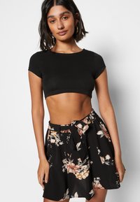 Top cropped preto com mangas curtas, combinado com uma saia floral preta com uma cintura larga e um cinto amarrado. Padrões florais em rosa e creme.