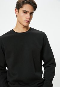 Sudadera negra de manga larga con cuello redondo. Está hecha de un suave tejido de algodón, con una textura lisa y un corte relajado.