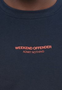 Navy blue cotton t-shirt with round neckline, featuring red printed text that reads "WEEKEND OFFENDER" and "ADMIT NOTHING."