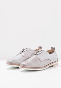 Chaussures à lacets en cuir argenté avec une texture perforée, bout arrondi et semelle blanche avec un subtil accent en bois.