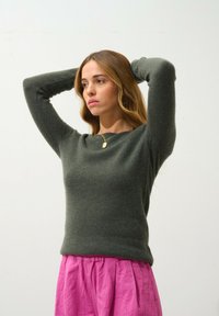 Olijfgroen wollen trui met lange mouwen, een ronde halslijn en een aansluitende vorm, gecombineerd met een geplooide roze rok voor contrast.