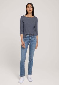 Camiseta de rayas en azul marino y blanco de manga larga combinada con jeans de mezclilla azul claro y zapatillas blancas; presenta un cuello redondo y un diseño ajustado.