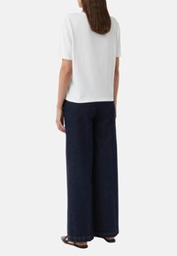 Weißes Baumwoll-T-Shirt mit kurzen Ärmeln, kombiniert mit weit geschnittenen, dunkelblauen Jeans, die ein sauberes, minimalistisches Design und eine gerade Passform aufweisen.