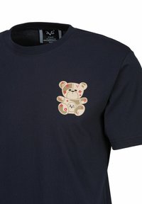 Navyblauw katoenen t-shirt met een beige teddybeer graphic met rode bloemaccenten en geometrische vormen op de linkerborst.