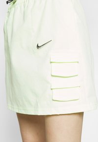 Jasnozielone szorty cargo z elastycznym pasem. Zawierają czarne logo Nike oraz dwie przednie kieszenie naszywane, każda z klapką.