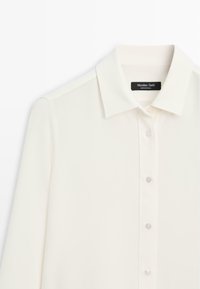 Krémová halenka s klasickým límcem, zapínáním na knoflíky a měkkou texturou. Vnitřní štítek s označením značky "Massimo Dutti".