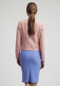 Fitted rosa blazer med långa ärmar, i kombination med en blå texturerad pennkjol. Bakvyen framhäver rena linjer och en strukturerad silhuett.