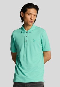 Polo de color turquoise claro con tapeta de tres botones, mangas cortas y un sutil logotipo bordado en el pecho. Tejido de algodón suave.