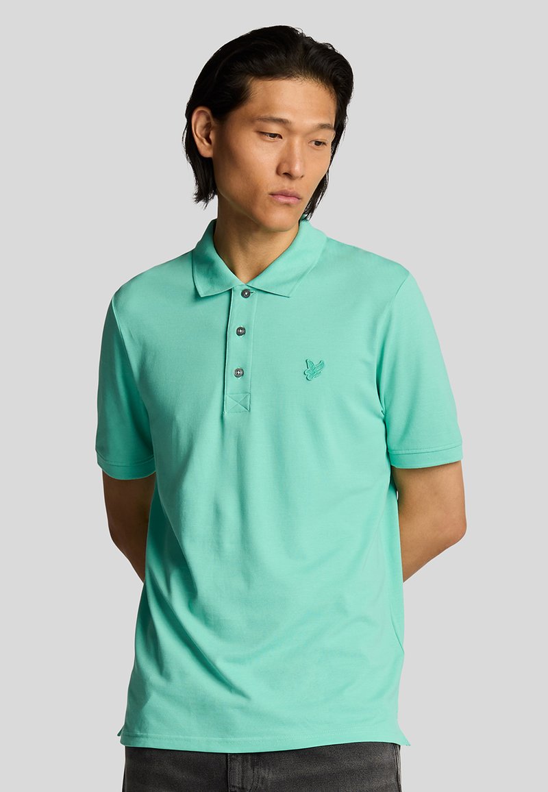 Polo de color turquoise claro con tapeta de tres botones, mangas cortas y un sutil logotipo bordado en el pecho. Tejido de algodón suave.