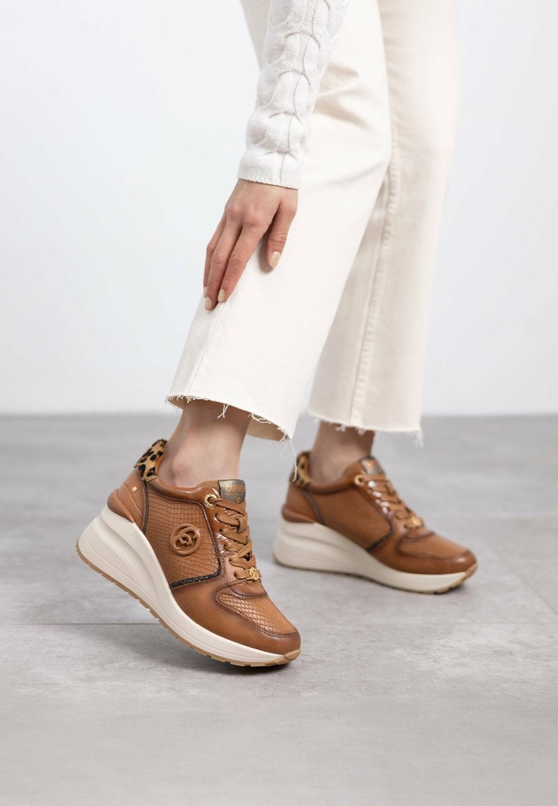 Zapatillas de piel marrón con un diseño texturizado, que cuentan con un acento de estampado de leopardo y una suela cuña blanca acolchada. Cierre con cordones.