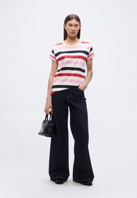 Ριγέ βαμβακερό T-shirt σε αποχρώσεις του ρόζ, κόκκινου και ναυτικού μπλε. Κλασική εφαρμογή με κοντά μανίκια. Συνδυασμένο με σκούρο τζιν καμπάνα και μικρή μαύρη τσάντα χειρός.