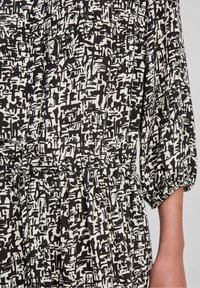 Zwart-wit jurk met patroon, met een losse pasvorm, geplooid bij de taille en met pofmouwen. Gladde stoftextuur en abstract ontwerp.