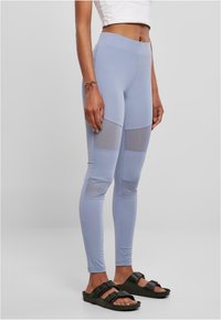 Lys blå leggings med mesh-paneler og et tettsittende design. Glatt tekstur med bred midje, kombinert med svarte sandaler.