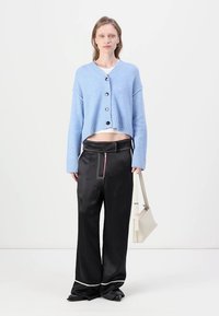 Light blue cropped cardigan with buttons, worn over a white top, paired with black satin wide-leg pants featuring contrasting white stitching.