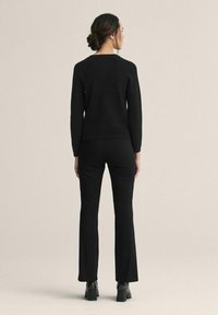 Svart tröja med rund hals och långa ärmar, ihop med svarta utsvängda byxor och klackade ankelstövlar. Enkelt, slätt material.