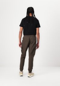 Cargo pants in dark olive green, made from lightweight fabric; features elastic waistband, side pockets, and tapered ankles. Black t-shirt worn.