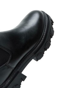 Botte ankle en cuir noir avec une finition lisse, des panneaux latéraux élastiques et une semelle texturée robuste avec des crampons proéminents.