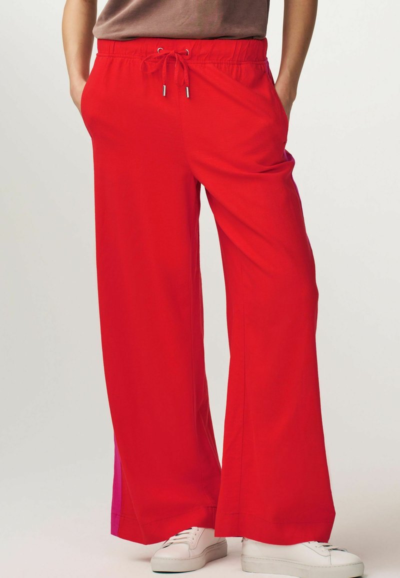 Pantalones de pierna ancha rojos, hechos de un tejido ligero, con una cintura elástica con cordón y bolsillos laterales. Acentuados con un panel rosa.