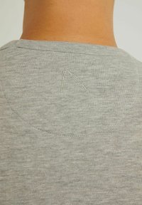 T-shirt in cotone grigio con scollo rotondo e dettaglio ricamato a forma di 'A' sul retro. Il tessuto ha un aspetto leggermente testurizzato.