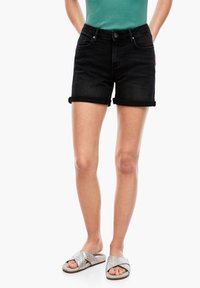 Černé džínsové šortky s ohrnutým lemem, se předními kapsami a zipem. Vybaveny stříbrnými pletenými sandály na klínku.
