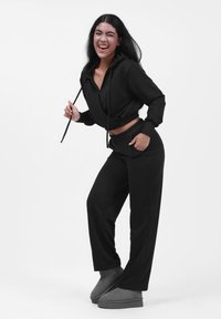 Sudadera negra recortada con cordones, combinada con pantalones negros a juego. La modelo lleva botas de tobillo grises. Textura suave; corte relajado.