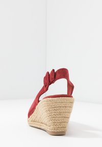 Rode suède wedge sandaal met een gestructureerde jute zool, voorzien van een slingback band en een strikaccent. Achteraanzicht weergegeven.