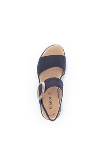 Sandale bleu marine en suède, avec deux larges sangles et un accent métallique rond. La semelle est marron clair avec le logo de la marque.