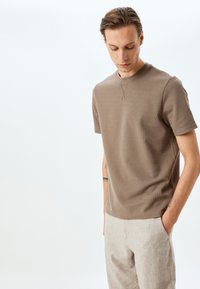 Brun ribbet kortærmet t-shirt med rund halsudskæring og subtil syning. Sammen med lyse linbukser.