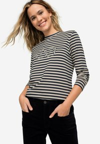 Pruhovaný dlouhý rukáv v námořnické modré a béžové barvě s grafickým designem na přední straně. Vyrobeno z měkké látky; v kombinaci s černými kalhotami.