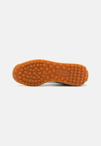 Semelle de chaussure en caoutchouc orange avec motif de bande de roulement circulaire et logo Puma embossé au centre, vue de dessous.