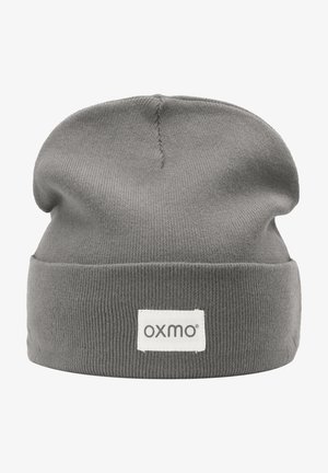 Graue Strickmütze mit umgeschlagenem Saum und einem kleinen weißen Etikett mit schwarzem Text. Die Textur ist durchgehend gerippt und glatt.