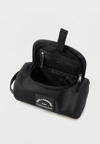 Black nylon toiletry bag with a rounded shape, featuring a zippered closure, interior pockets, and a branded patch on the front.